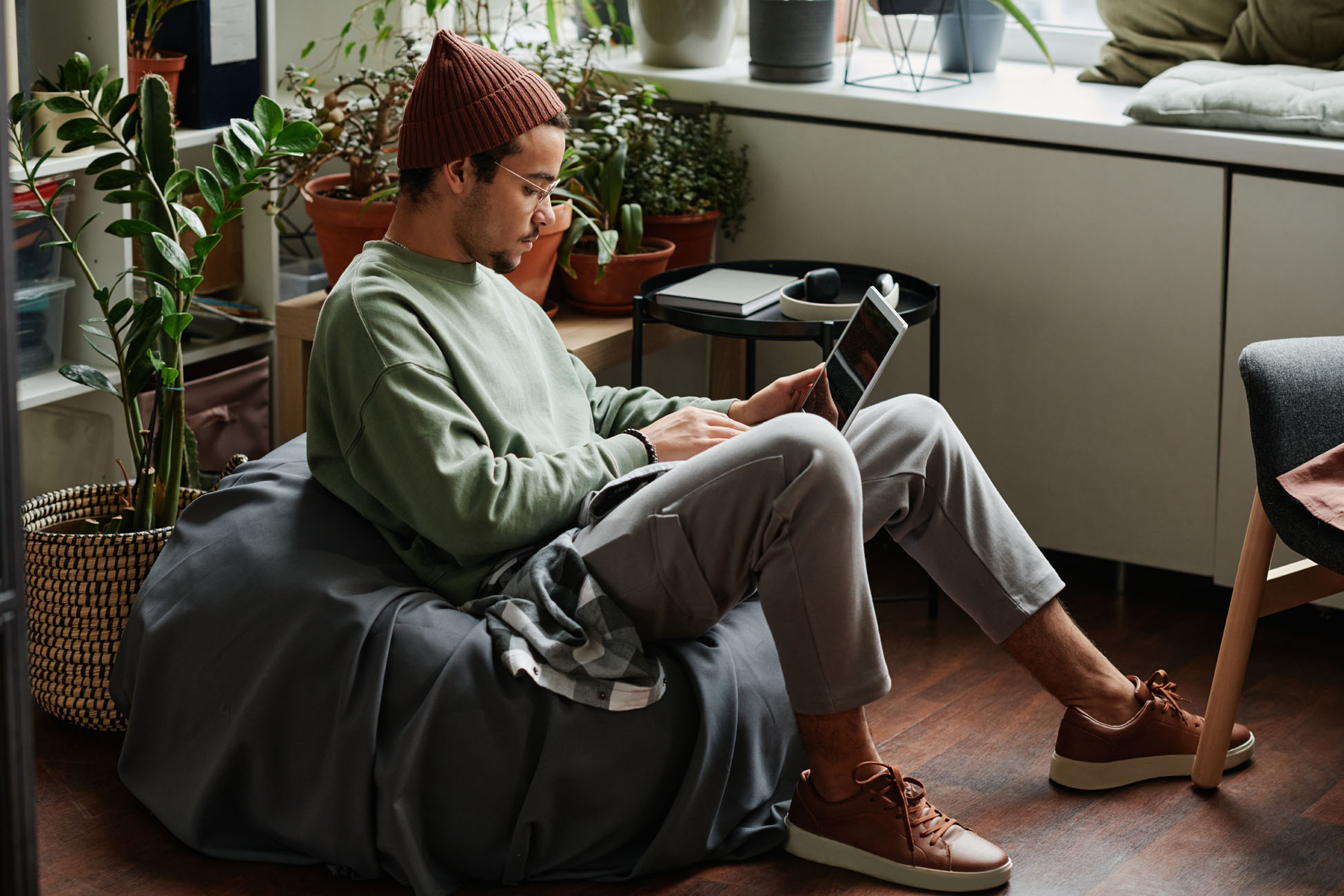 Young serious webdesigner with laptop concentrating on network while sitting in comfortable armchair in office with many green plants